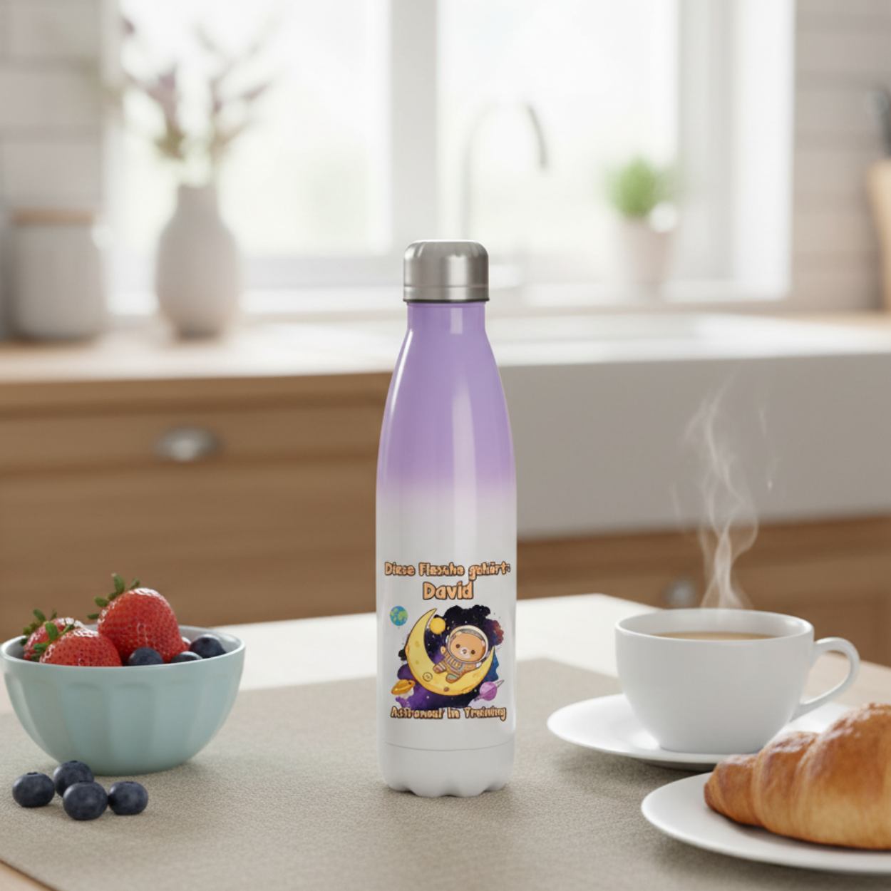 Detailaufnahme des bunten Astronauten-Motivs auf einer weißen Kinder-Trinkflasche mit glänzendem Edelstahlverschluss.